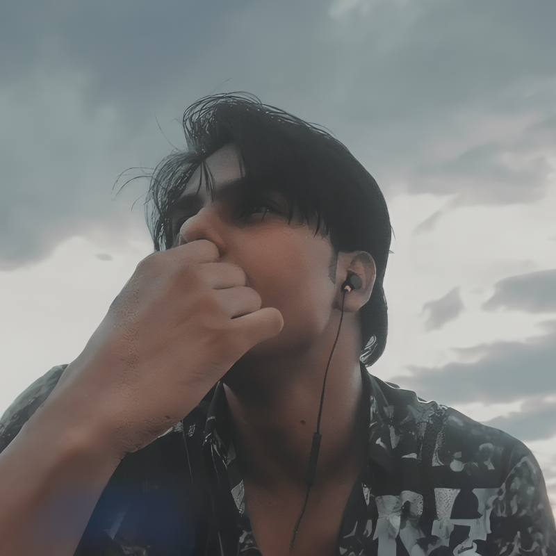 Swayam looking at the distance to the left of the camera. He is wearing headphones and has his hand partly covering his face. The sky behind him is cloudy and gray.